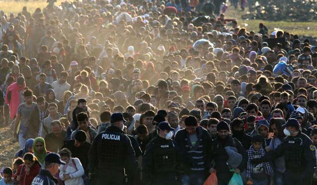 migrants and refugees are escorted by slovenian soldiers and police officers as they walk towards a refugee camp after crossing the croatian slovenian border near rigonce slovenia on october 26 2015 photo afp