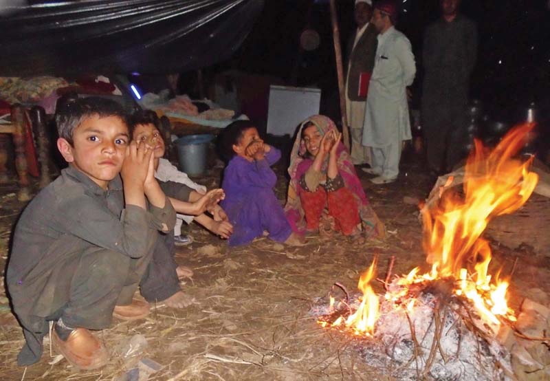 children sit besides a fire to keep themselves warm in a temporary shelter in lower dir photo inp