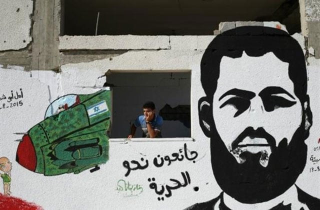 a palestinian youth stands behind a wall sprayed with a graffiti depicting 31 year old muhammed allan photo afp a palestinian youth stands behind a wall sprayed with a graffiti depicting 31 year old muhammed allan photo afp