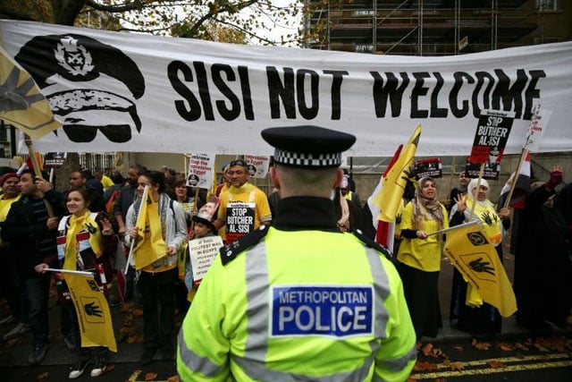 a police officer stands opposite protesters opposed to egyptian president sisi holding flags bearing the four finger symbol associated with those killed in the crackdown on a protest camp in cairo in 2013 photo afp