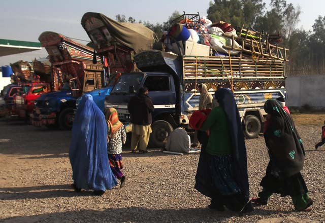 an afghan refugee family walks past trucks loaded with their belongings as they prepare to go back to afghanistan with others at the unhcr office on the outskirts of peshawar february 13 2015 photo reuters