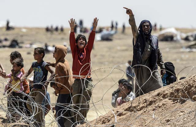 in a picture taken from akcakale in turkey syrian refugees gesture as they ask for water at the turkish border near the syrian town of tal abyad on june 13 2015 photo afp