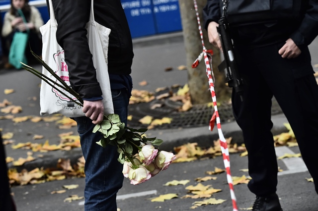 a civilian holds flowers next to a policeman near the rue de charonne in paris on november 14 2015 following a series of coordinated attacks in and around paris late friday which left more than 120 people dead photo afp