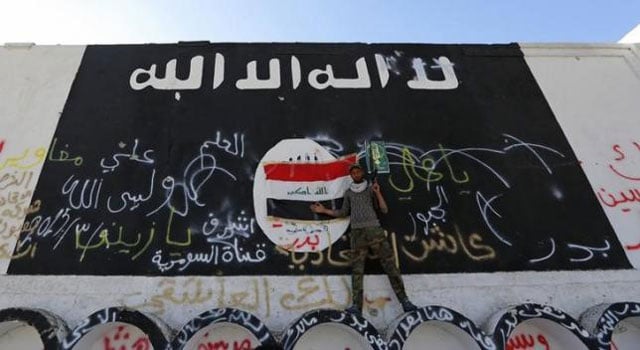 a member of militias known as hashid shaabi stands next to a wall painted with the black flag commonly used by islamic state militants in the town of al alam on march 10 2015 photo reuters