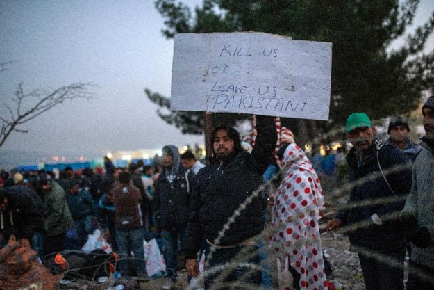 a migrant from pakistan holds a placard as he waits with other migrants and refugees to cross the greek macedonian border near gevgelija on november 20 2015 photo afp