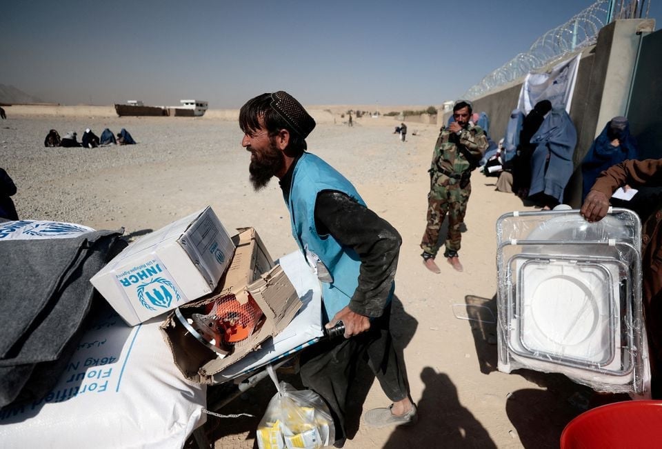 an unhcr worker pushes a wheelbarrow loaded with aid supplies for a displaced afghan family outside a distribution centre as a taliban fighter secures the area on the outskirts of kabul afghanistan october 28 2021 photo reuters file
