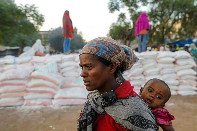 a woman carries an infant as she queues in line for food at the tsehaye primary school which was turned into a temporary shelter for people displaced by conflict in the town of shire tigray region ethiopia march 15 2021 photo reuters