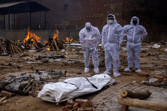 men wearing protective suits stand next to the body of their relative who died from the coronavirus disease covid 19 before her cremation at a crematorium ground in new delhi india may 4 2021 photo reuters