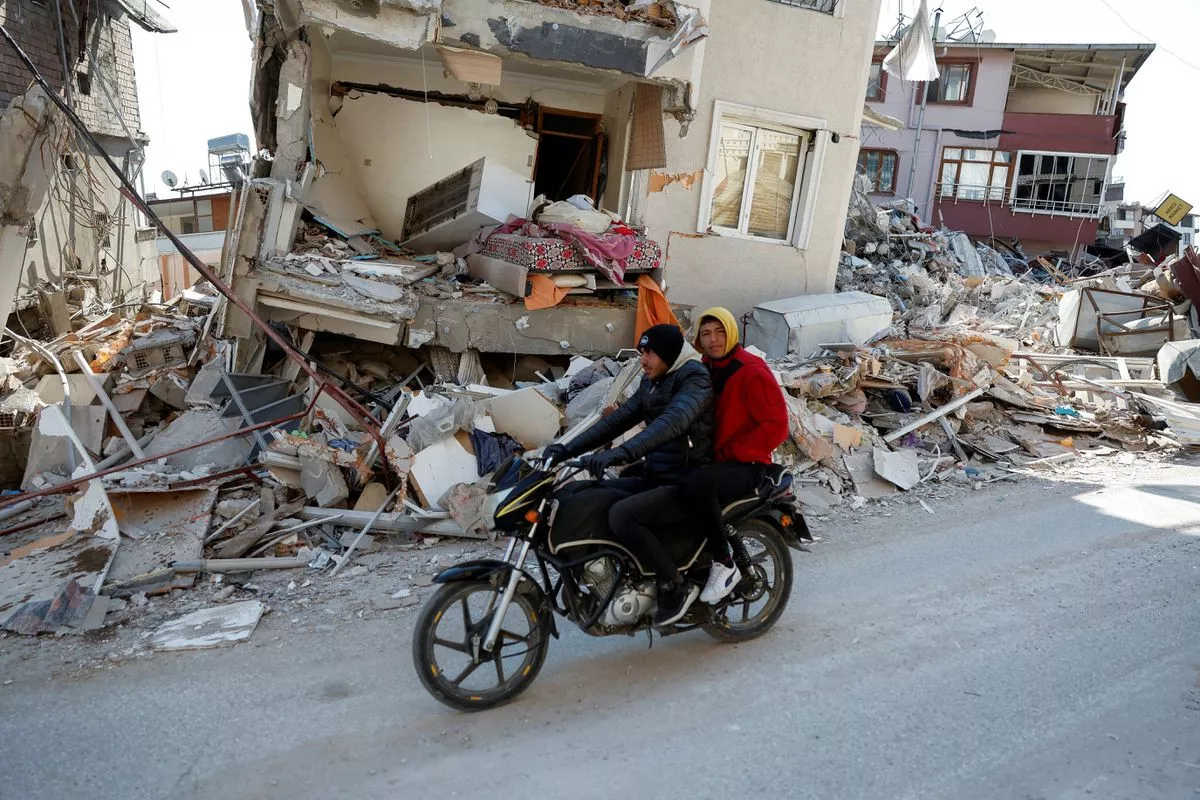 men on a scooter ride past a destroyed home with a bed hanging out in the aftermath of a deadly earthquake in hatay turkey february 14 2023 photo reuters men on a scooter ride past a destroyed home with a bed hanging out in the aftermath of a deadly earthquake in hatay turkey february 14 2023 photo reuters