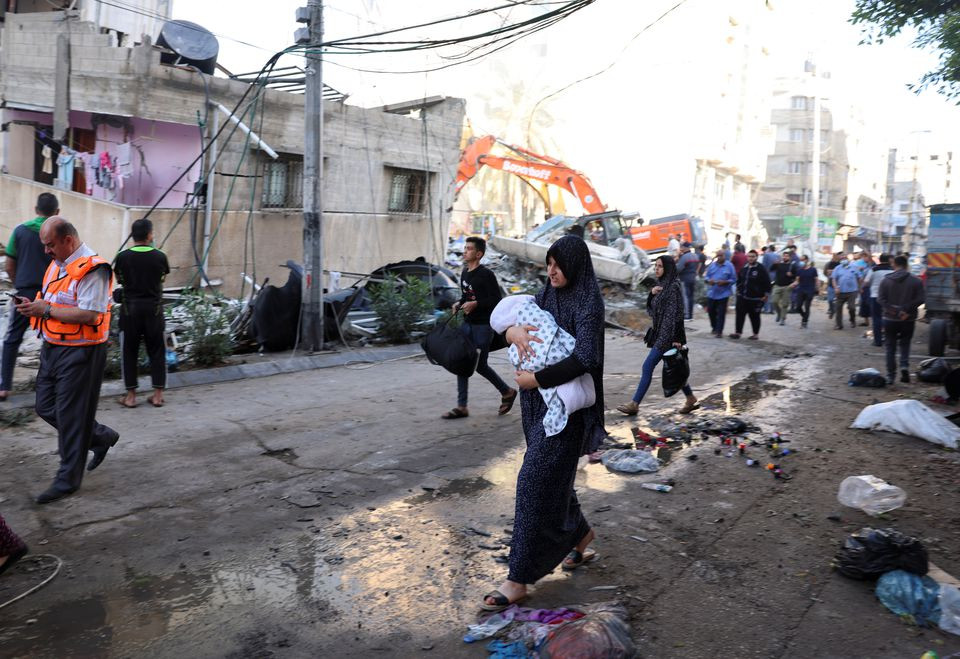 people walk past debris in a street at the site of israeli air strikes in gaza city may 16 2021 photo reuters