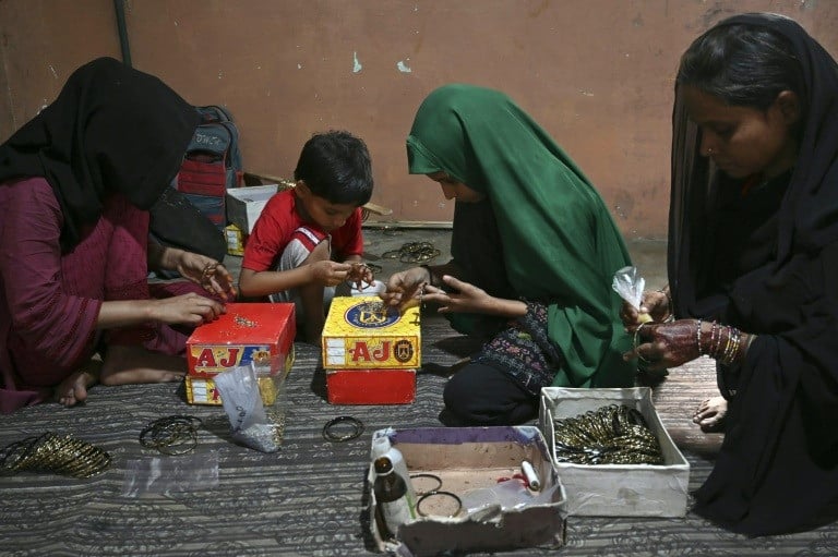 Worker Saima Bibi (R) along with her children, adds decorative elements to glass bangles at a home workshop in Hyderabad. PHOTO: AFP
