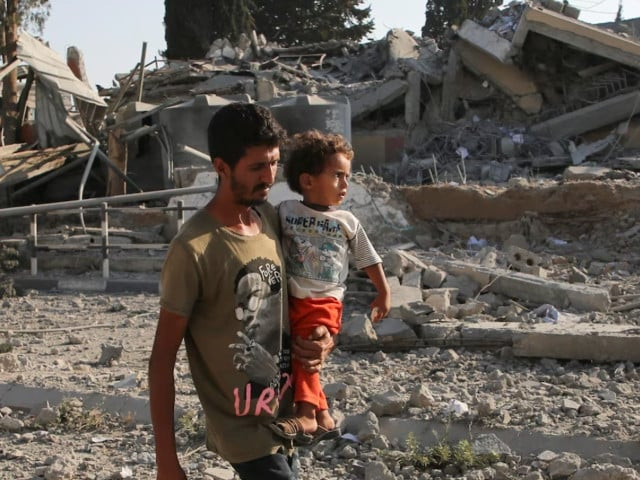 a palestinian man carries a child while walking near rubble following an israeli strike on a school sheltering displaced people amid the israel hamas conflict in khan younis in the southern gaza strip june 27 2024 photo reuters