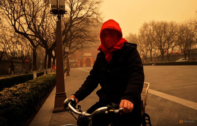 A woman cycles with her head covered during morning rush hour as Beijing, China, is hit by a sandstorm, March 15, 2021. PHOTO: REUTERS