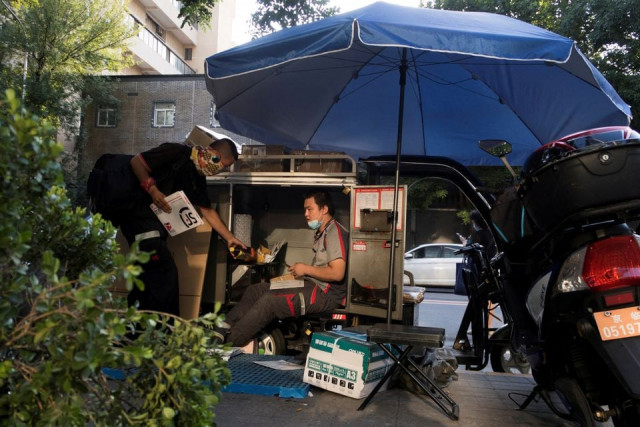 a delivery driver sorts parcels as he sits in the trunk of his electric tricycle following an outbreak of the coronavirus disease covid 19 in beijing china august 21 2020 reuters a delivery driver sorts parcels as he sits in the trunk of his electric tricycle following an outbreak of the coronavirus disease covid 19 in beijing china august 21 2020 reuters