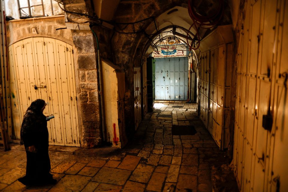 a woman reads in a commercial thoroughfare which is closed in protest of an israeli clampdown on jerusalem s outlying shuafat refugee camp after a palestinian gunman carried out a deadly attack on a military checkpoint in jerusalem s old city october 12 2022 reuters ammar awad