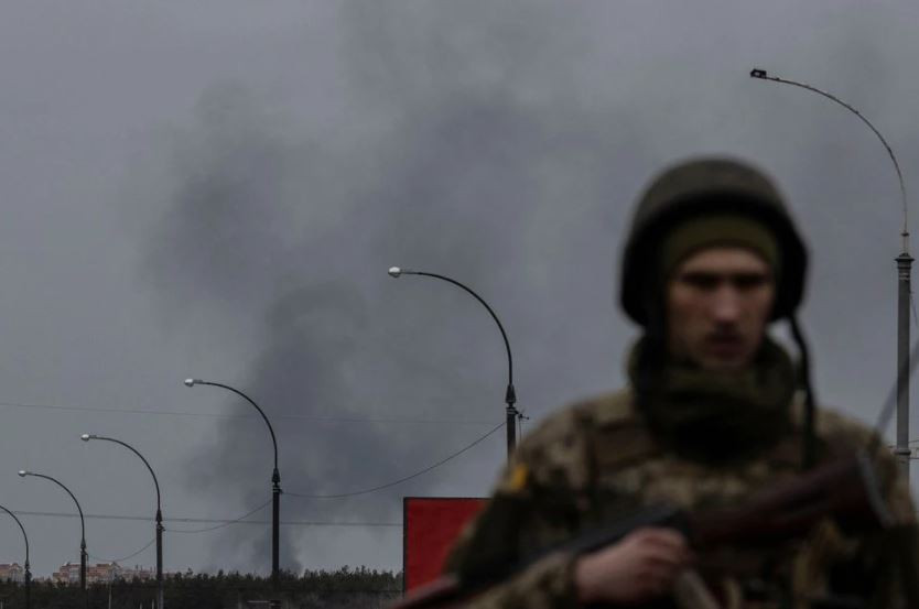 smoke rises as a service member of the ukrainian armed forces stands by the only escape route used by locals to evacuate from the town of irpin after days of heavy shelling while russian troops advance towards the capital in irpin near kyiv ukraine march 7 2022 photo reuters