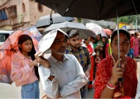 a man uses a newspaper as others use umbrellas to protect themselves from the heat as they wait to vote outside a polling station during the fifth phase of india s general election in howrah district of the eastern state of west bengal india may 20 2024 reuters sahiba chawdhary