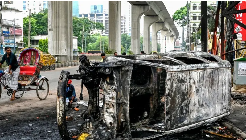 passersby look at a burnt vehicle along a street amid anti government protests in dhaka on august 5 2024 afp