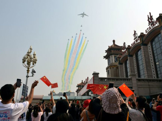 people hold their mobile phones and chinese flags as military aircraft fly in formation during the military parade marking the 70th founding anniversary of people s republic of china at a railway station in beijing china october 1 2019 photo reuters