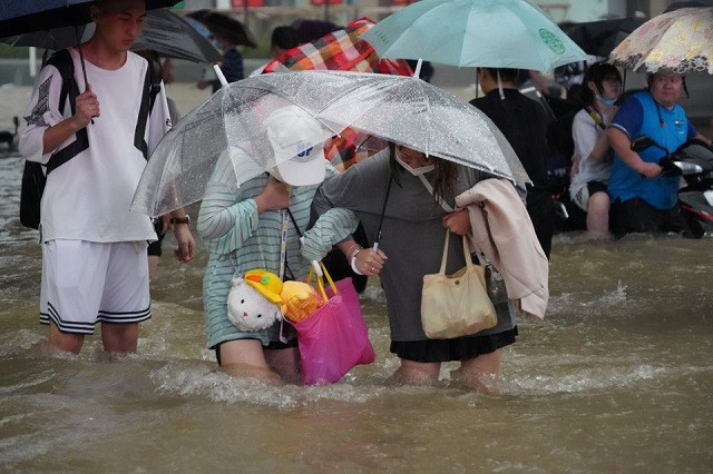 Residents, holding umbrellas amid heavy rainfall, wade through floodwaters on a road in Zhengzhou, Henan province, China July 20, 2021. PHOTO: REUTERS