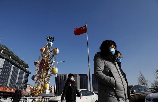 people wearing face masks walk past a chinese flag following new cases of the coronavirus disease covid 19 in the country in beijing china january 11 2021 photo reuters file