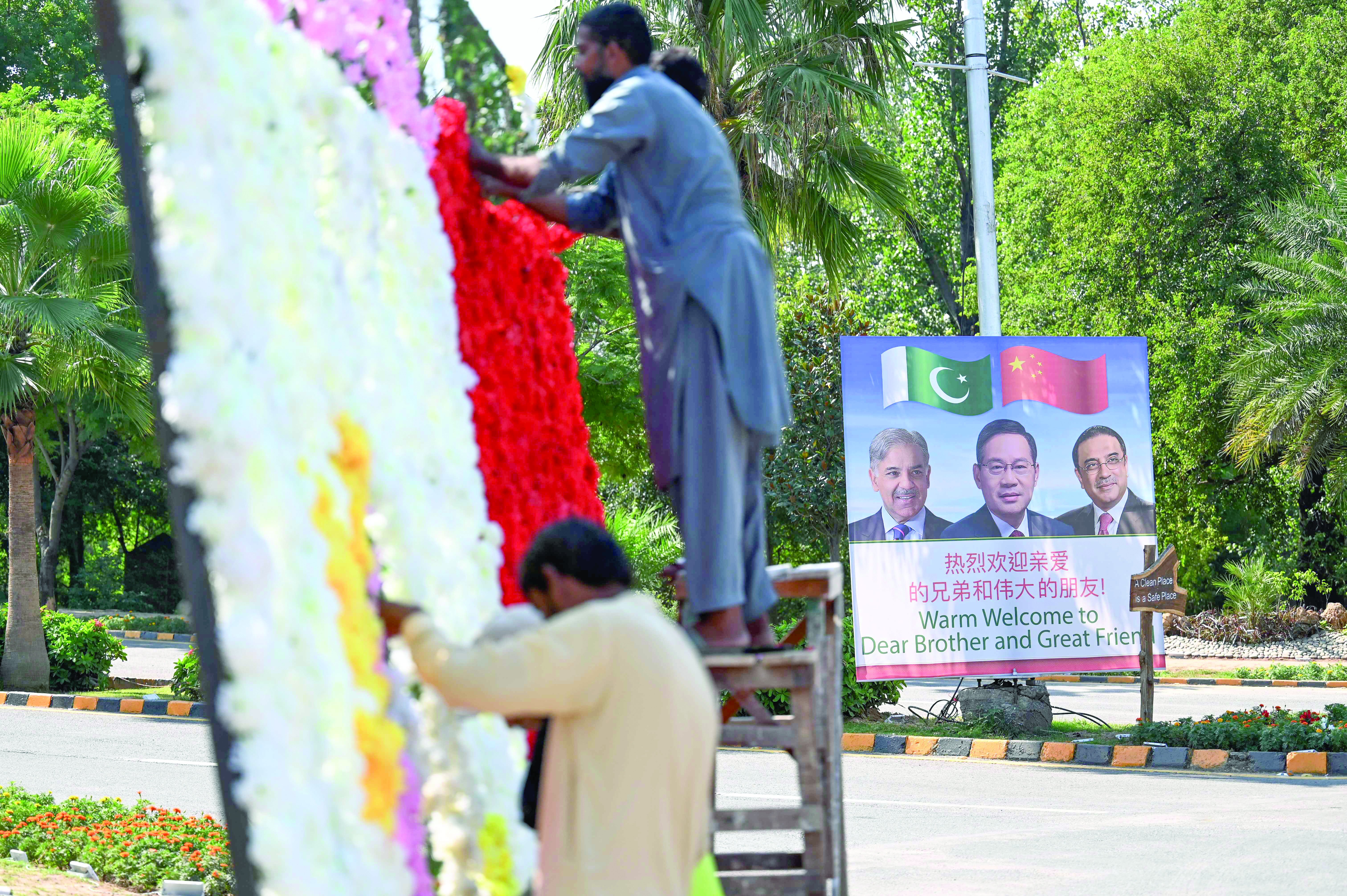 workers decorate a street near a billboard featuring images of china s premier li qiang prime minister shehbaz sharif and president asif ali zardari in islamabad photo afp