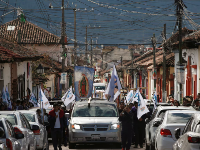 People walk next to a hearse carrying the coffin with the body of priest Marcelo Perez, through the streets in San Cristobal de las Casas, where he was killed on Sunday after officiating a mass, in San Cristobal de las Casas, in the southern state of Chiapas, Mexico, October 20, 2024. REUTERS/Gabriela Sanabria