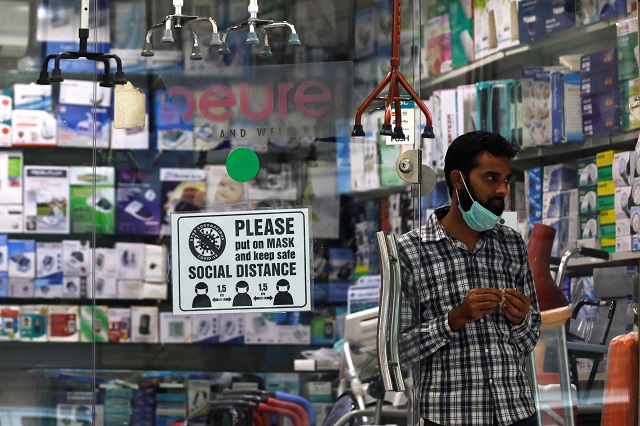 a man with a mask on his chin stands at the entrance of his shop displaying a covid 19 precautionary sign for the customers in karachi photo reuters