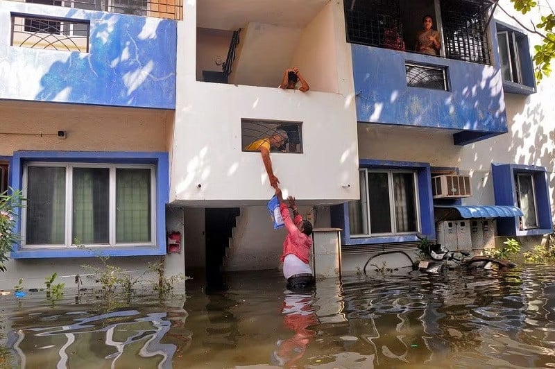 A volunteer offers food to a resident after his house got partially submerged following heavy rains due to Cyclone Michaung, in Chennai, India, December 6, 2023. PHOTO: REUTERS