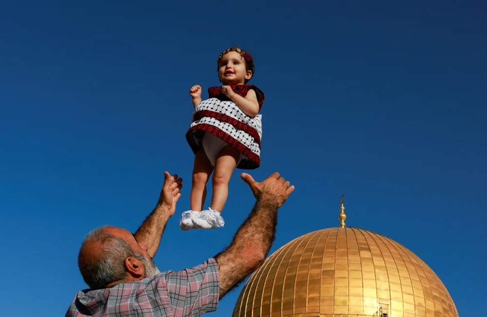 A man throws a girl in the air as Palestinians gather at the Al-Aqsa Mosque compound. PHOTO: REUTERS