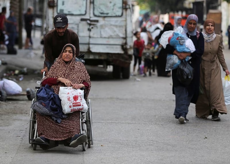 A Palestinian man assists a woman in a wheel chair carrying her belongings as they travel to flee Rafah due to an Israeli military operation, in Rafah, in the southern Gaza Strip, May 28, 2024. PHOTO: REUTERS