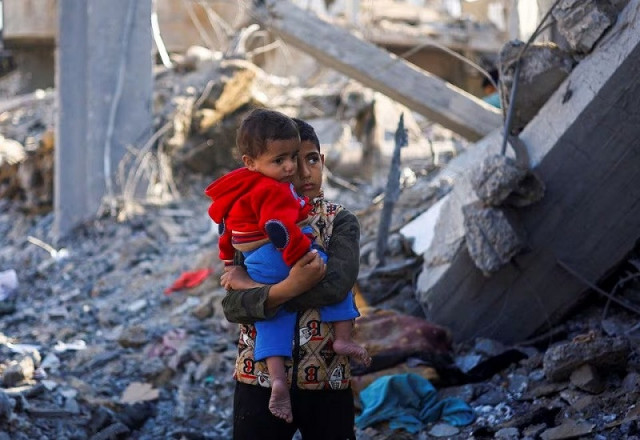 a palestinian boy carrying a baby stands at a site of israeli strikes in rafah in the southern gaza strip photo reuters