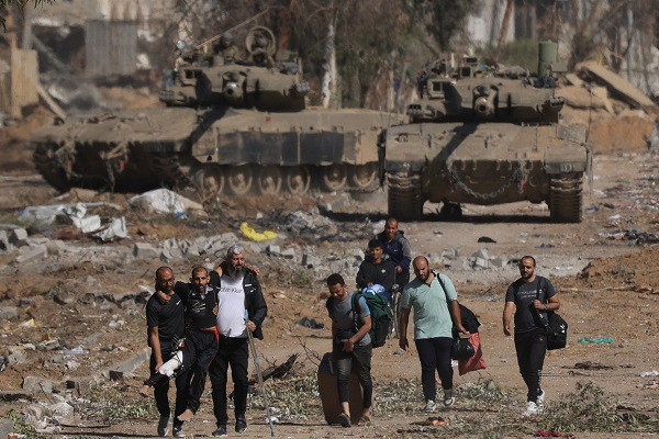 Palestinians fleeing the north along Salaheddine road help a man with a bandaged leg as they walk in front of Israeli army tanks in the Zeitoun district on the southern outskirts of Gaza City. PHOTO: AFP