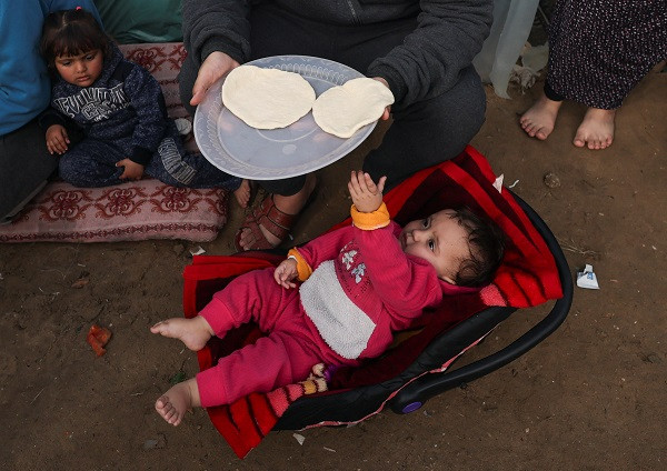 A baby reaches for a plate of food as displaced Palestinians, who fled their homes due to Israeli strikes, shelter at a tent camp. PHOTO: Reuters