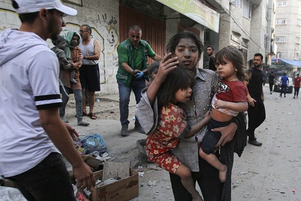 A Palestinian lady binds dual children as she stands on a travel in Gaza City following in Israeli airstrike. PHOTO: AFP