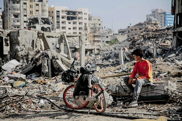 a palestinian youth sits next to his bicycle amid the rubble of destroyed buildings in gaza city on the northern gaza strip following weeks of israeli bombardment photo afp