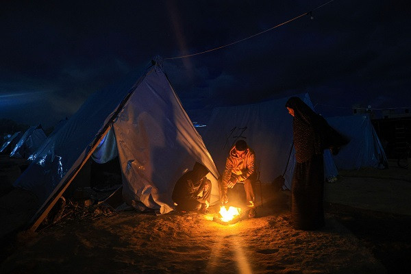 Displaced Palestinians gather next to shelter tents in Khan Yunis near the border fence between Israel and the southern Gaza Strip.  PHOTO: AFP
