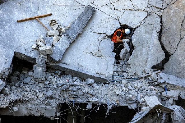 a palestinian civil defence member stands through a crack in a collapsed building hit by israeli bombardment while searching for victims and survivors in khan yunis in the southern gaza strip photo afp