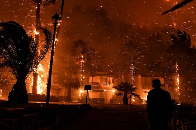 A local looks at flame rising among houses as a wildfire burns in the village of Schinos, near Corinth, Greece, May 19, 2021. PHOTO: REUTERS