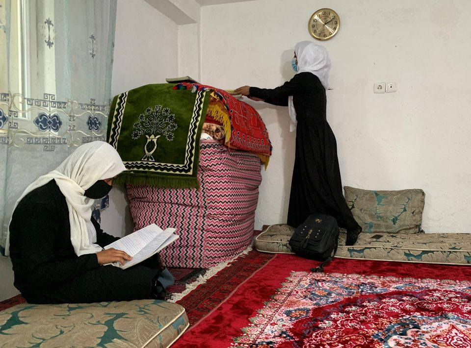 an afghan schoolgirl reads from her notebook as another unpacks her school bag inside a house in kabul afghanistan march 23 2022 reuters