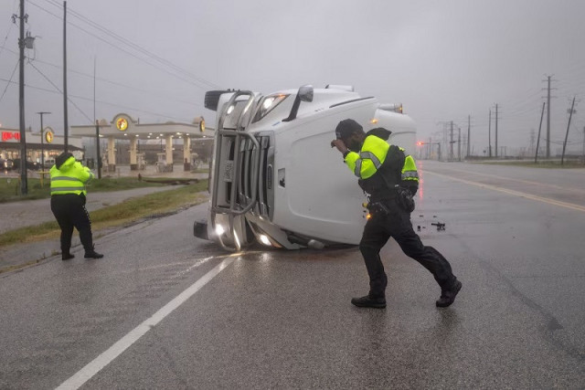 police officers struggle with fierce winds from hurricane beryl as they search an overturned semi trailer truck for occupants in freeport texas us july 8 2024 photo reuters