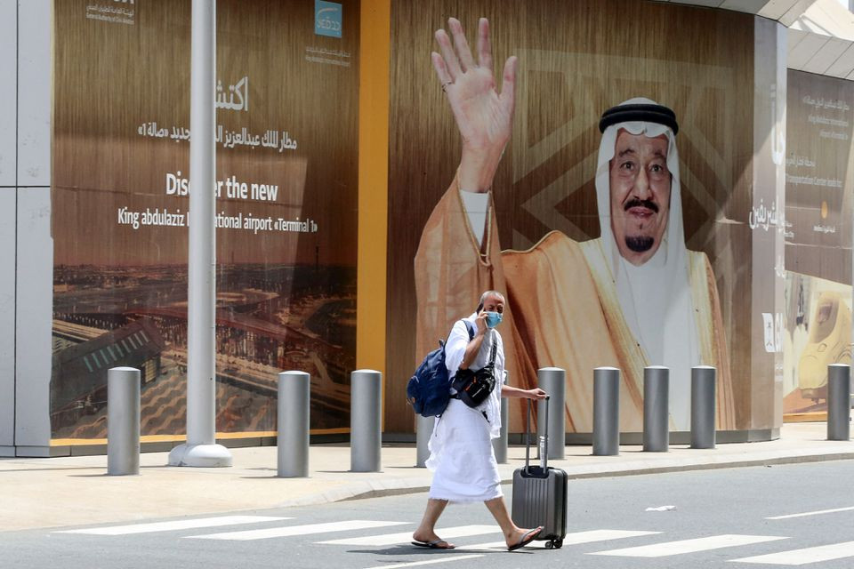 a muslim pilgrim wearing a white clothing walks past a picture of saudi king salman bin abdulazi at king abdulaziz international airport ahead of the annual haj pilgrimage in jeddah saudi arabia july 17 2021 photo reuters file