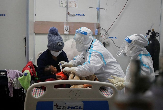 medical workers wearing personal protective equipment ppe check temperature of an infant whose mother is suffering from coronavirus disease covid 19 inside a care centre at an indoor sports complex amidst the spread of the disease in new delhi india january 5 2022 photo reuters