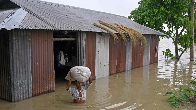 a man wades through floodwaters as he carries a sack of rice from his house deluged by heavy rain in morigaon district in assam india photo afp