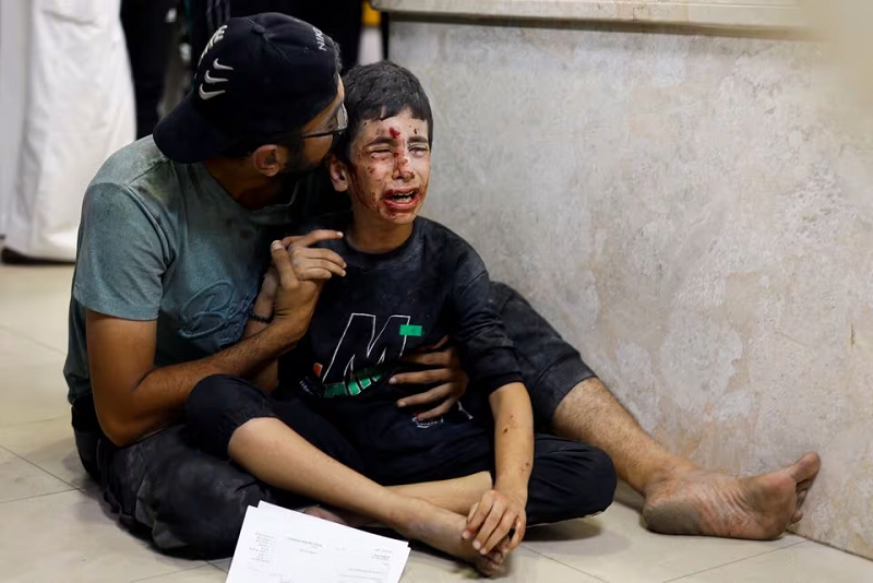A Palestinian man sits with a child wounded in an Israeli strike at Nasser hospital in Khan Younis in the southern Gaza Strip November 18, 2023. PHOTO: REUTERS