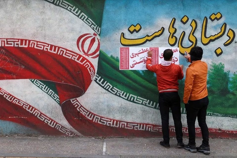 Iranian men put campaign posters on a wall during the last day of election campaigning in Tehran, Iran, February 28, 2024. PHOTO: REUTERS