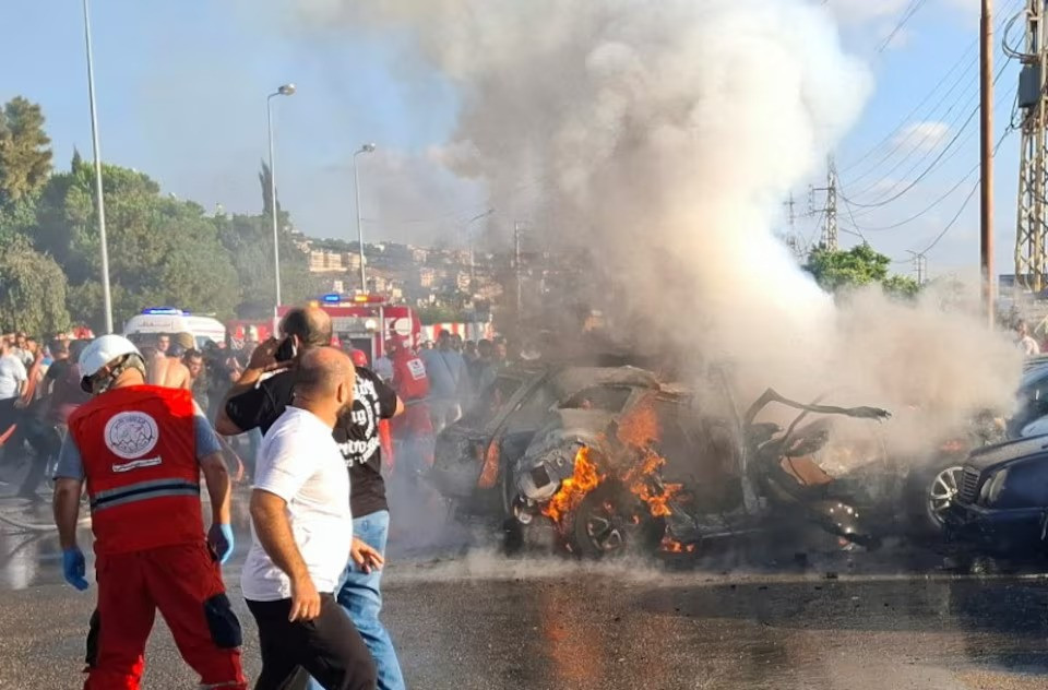 people and civil defence members stand near a burning car after an israeli airstrike targeted a car on the edge of lebanon s port city of sidon on august 9 2024 photo reuters