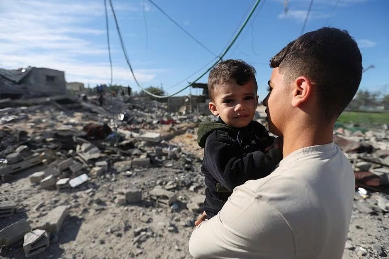 a palestinian holds a child as they look on at the site of an israeli strike on a house in rafah in the southern gaza strip december 16 2023 photo reuters