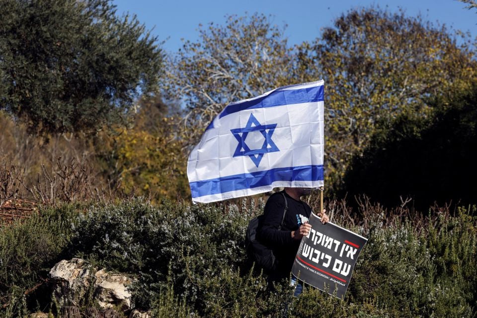 a man holds the national flag of israel and a sign that says in hebrew there is no democracy if there is occupation at a protest outside the knesset israel s parliament on the day the new right wing government is sworn in with benjamin netanyahu as prime minister in jerusalem december 29 2022 photo reuters ammar awad