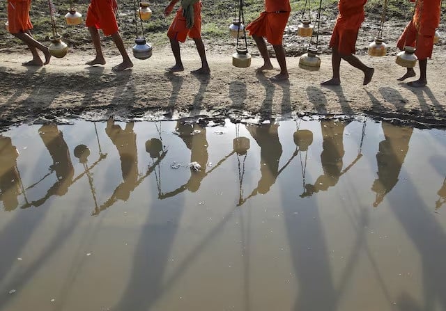 kanwarias or devotees of hindu god shiva carrying pitchers are reflected in a puddle as they walk after filling the pitchers with the water from the river ganges in allahabad india july 13 2015 photo reuters